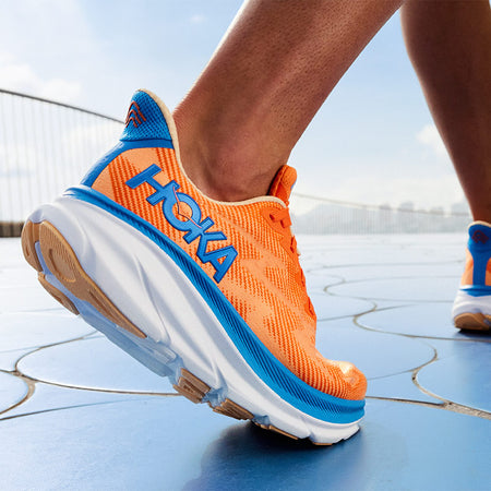 closeup of a person walking in orange and blue men's HOKA Clifton 9 running shoes