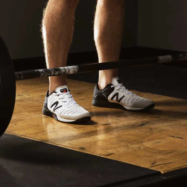 man with white new balance shoes standing in front of barbell