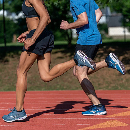 Two people running on red track court